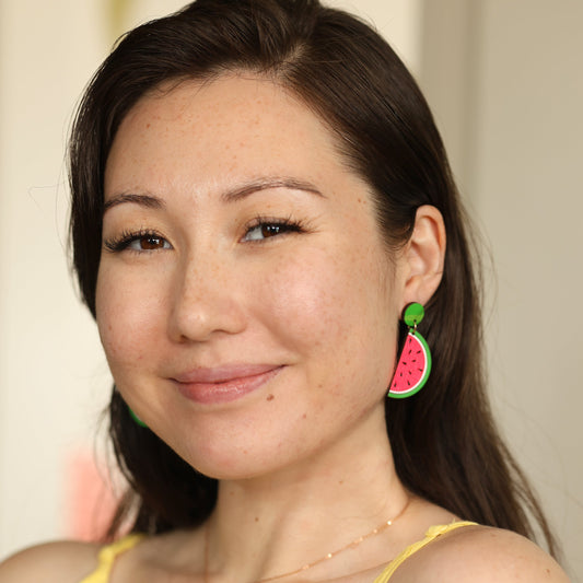 Woman smiling and wearing hand-painted watermelon stud dangle earrings by Le Chic Miami – vibrant accessory