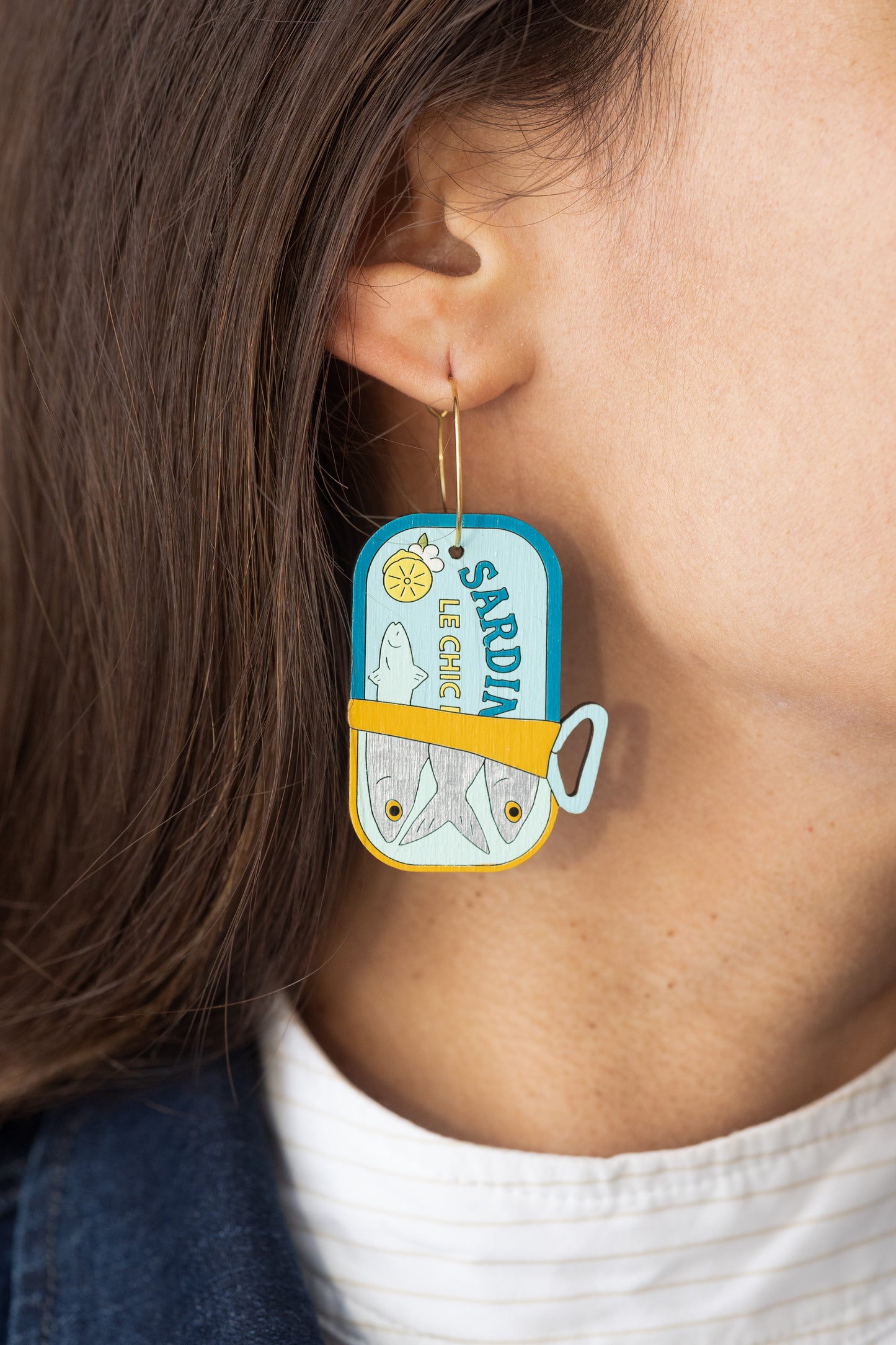 Close-up of Le Chic Miami wooden sardine can hoop earring worn by woman