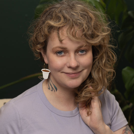 Woman wearing lilac shirt and hand-painted Cafecito Hoop earring shaped like a Cuban coffee cup by Le Chic Miami.