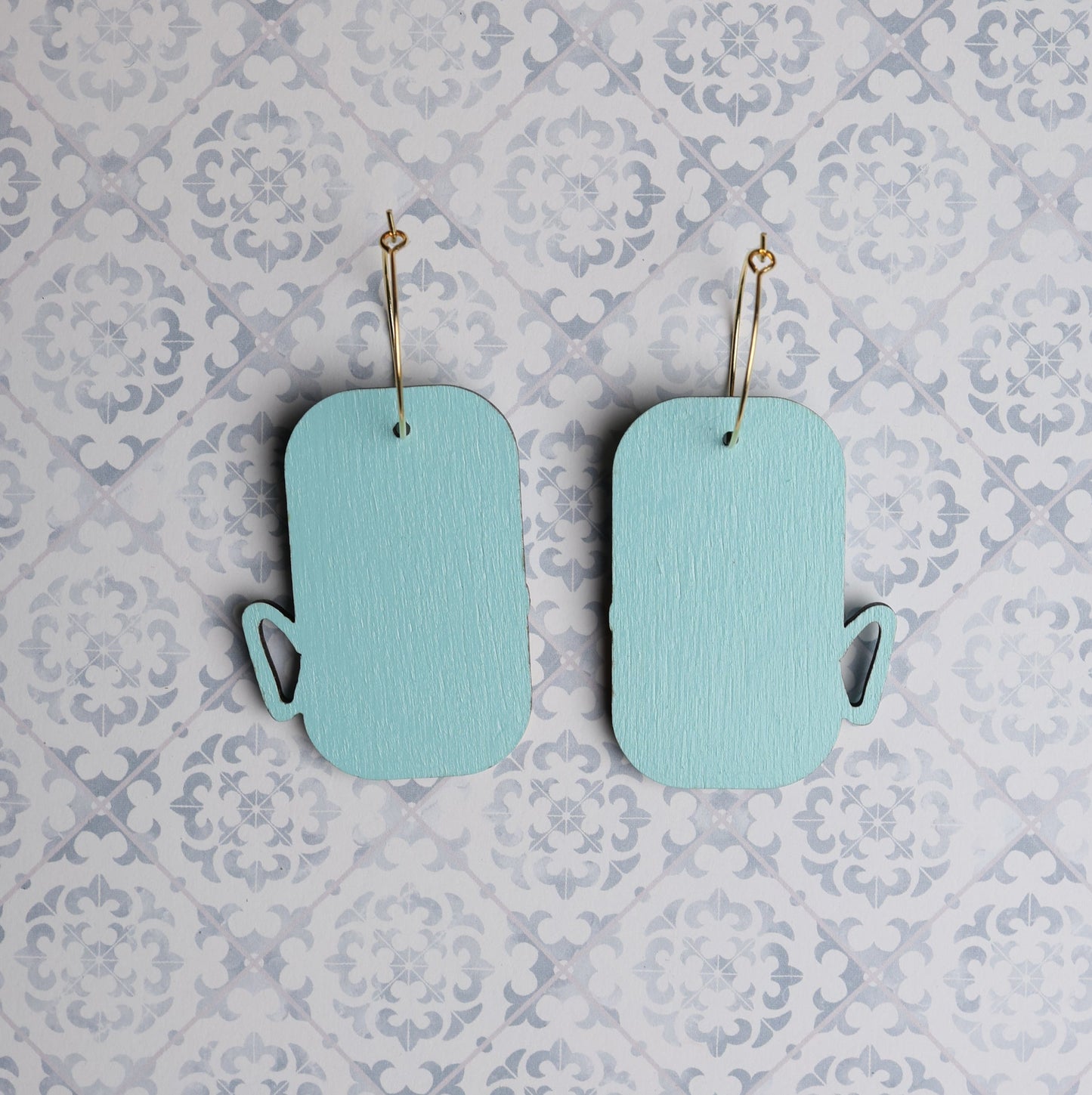 Back view of turquoise wooden sardine can earrings on patterned background